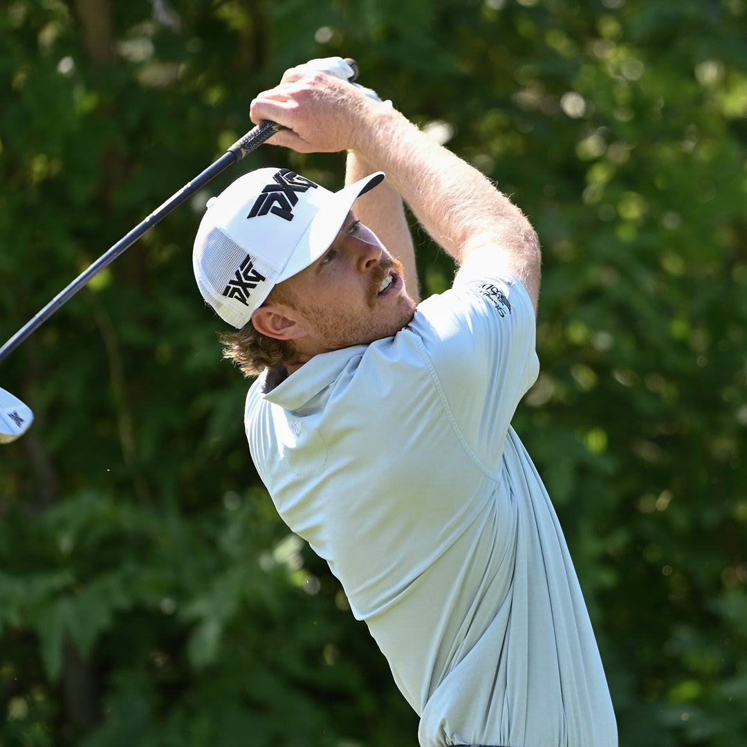 Pro Christian Banke wearing a PXG Hat and swinging a golf club on a golf course.