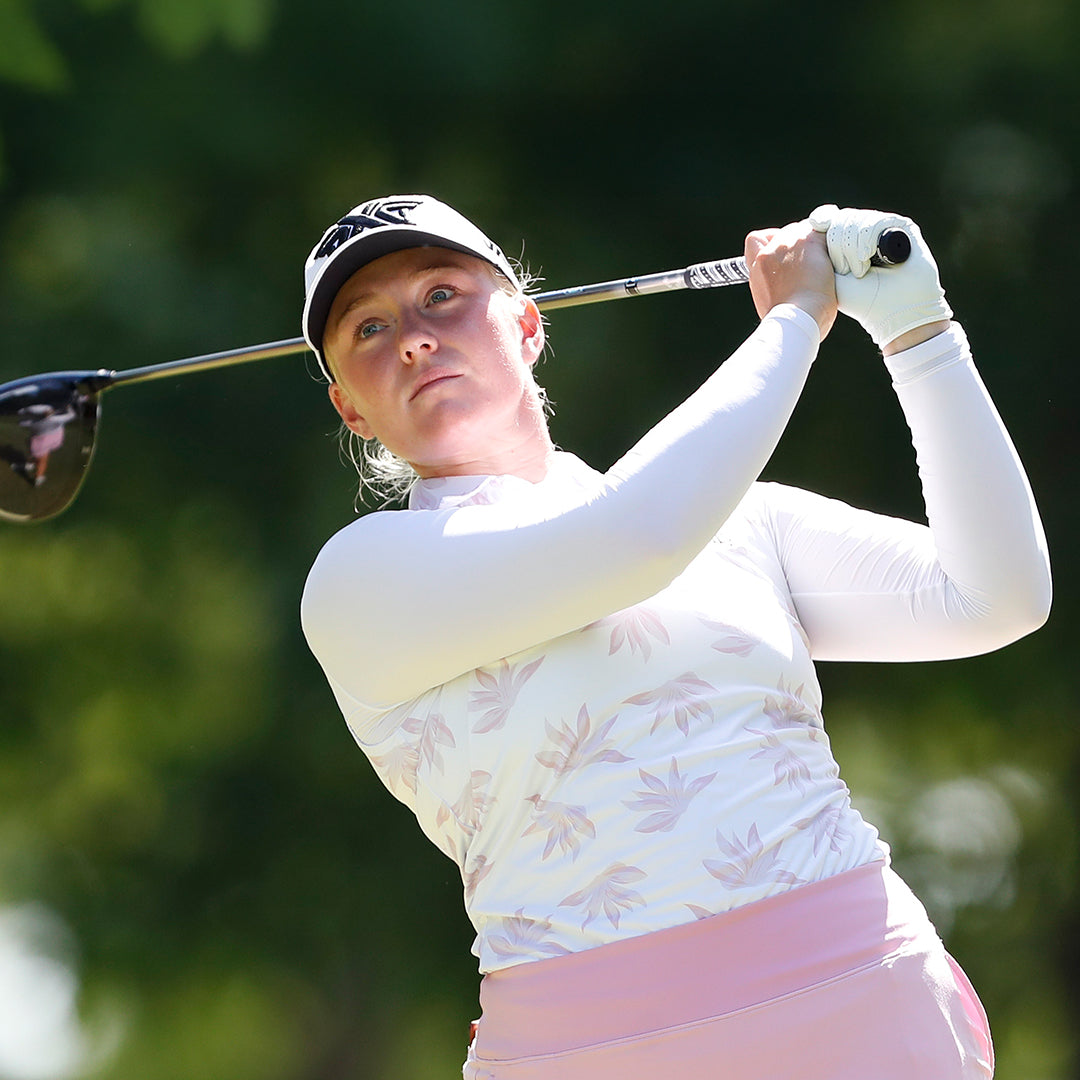 Pro Kaitlin Milligan wearing a PXG Hat and swinging a golf club on a golf course.