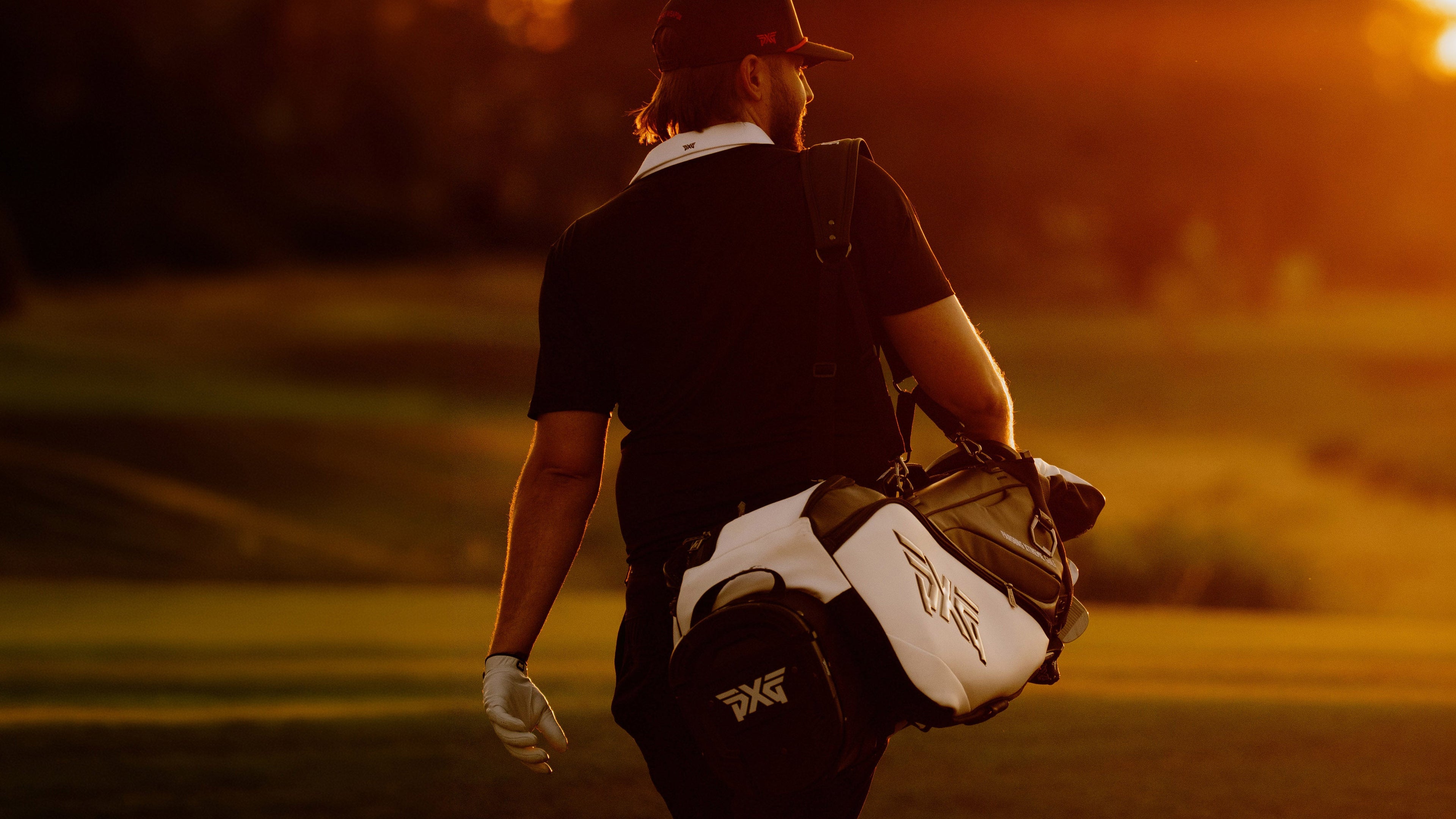 A golfer seen from behind on a golf course at sunset, carrying a white and black golf bag with a visible Callaway logo.
